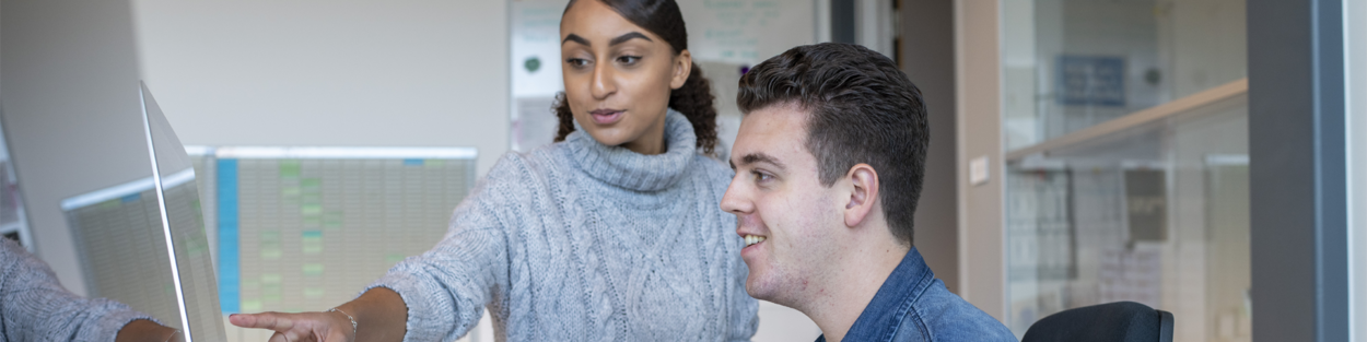 Een jongeman werkt op computer en een jonge vrouw kijkt mee